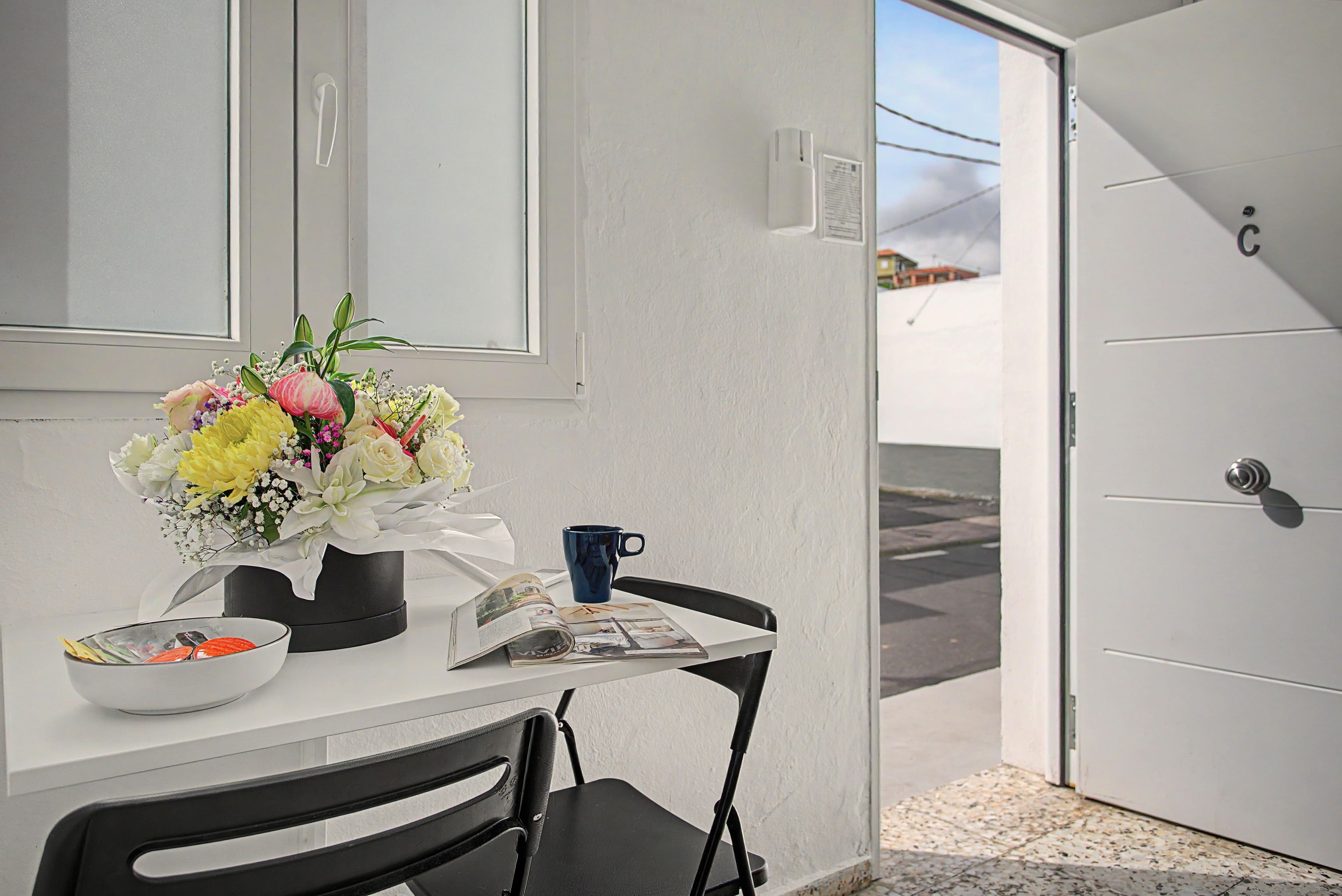 A table with a vase of flowers, a mug, and a bowl, a chair, and a door with a number.