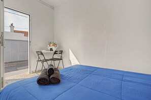 Une pièce comprenant un lit, deux chaises, une table avec un vase de fleurs et une vue sur un bâtiment à l’extérieur.