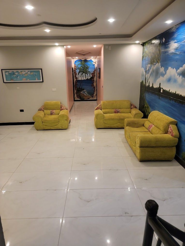 A lobby with a tiled floor, yellow armchairs, a mural, and a framed picture on the wall.