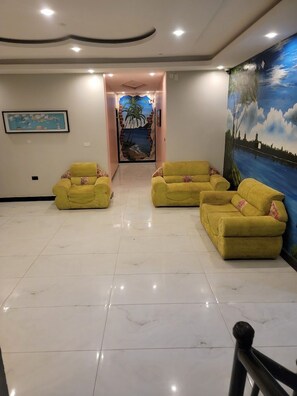 Un hall con suelo de baldosas, sillones amarillos, un mural y un cuadro enmarcado en la pared.