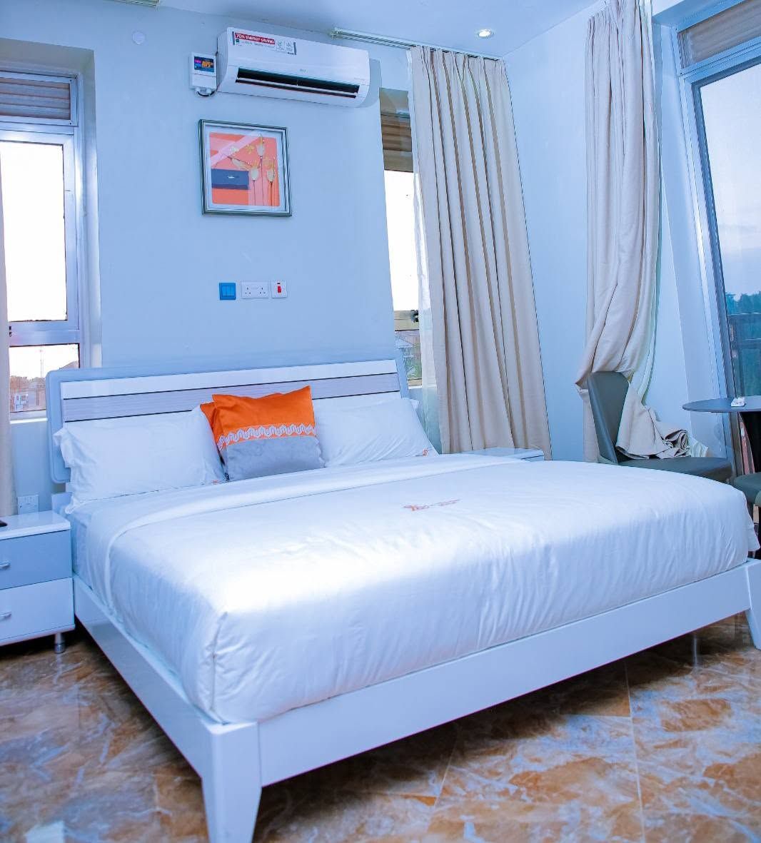 Una habitación de hotel con cama, mesita de noche, ventana con cortinas y un equipo de aire acondicionado.