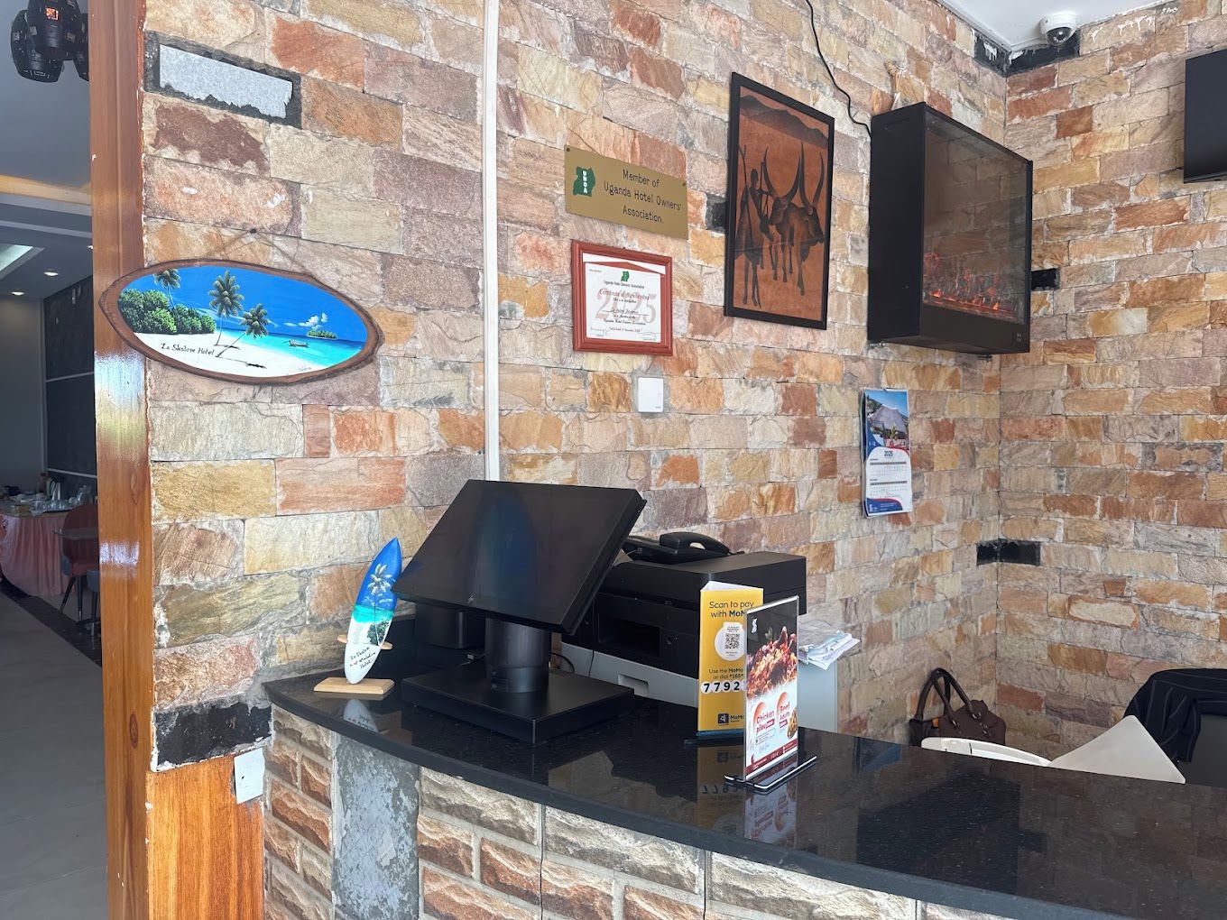Un mostrador de recepción con un fondo de pared de piedra, un certificado enmarcado y un televisor montado.