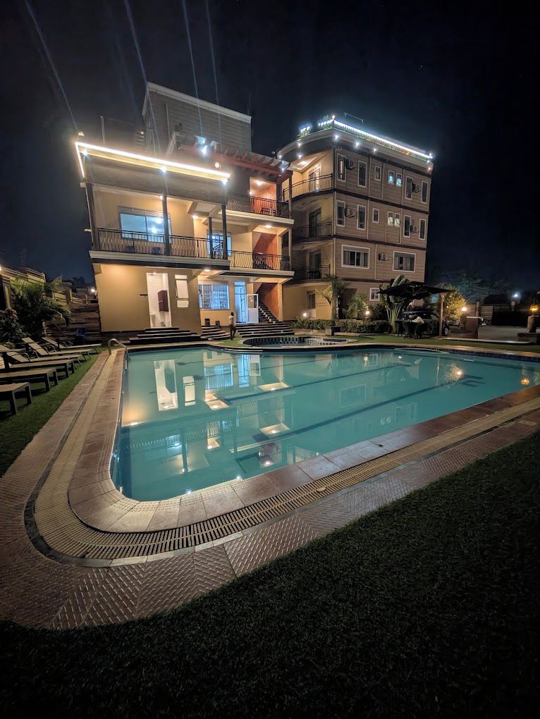 Una piscina con un deck circundante, un edificio de varios pisos con balcones y un exterior bien iluminado.