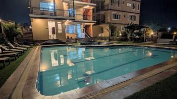 Una piscina con un deck circundante, un edificio de varios pisos con balcones y un exterior bien iluminado.