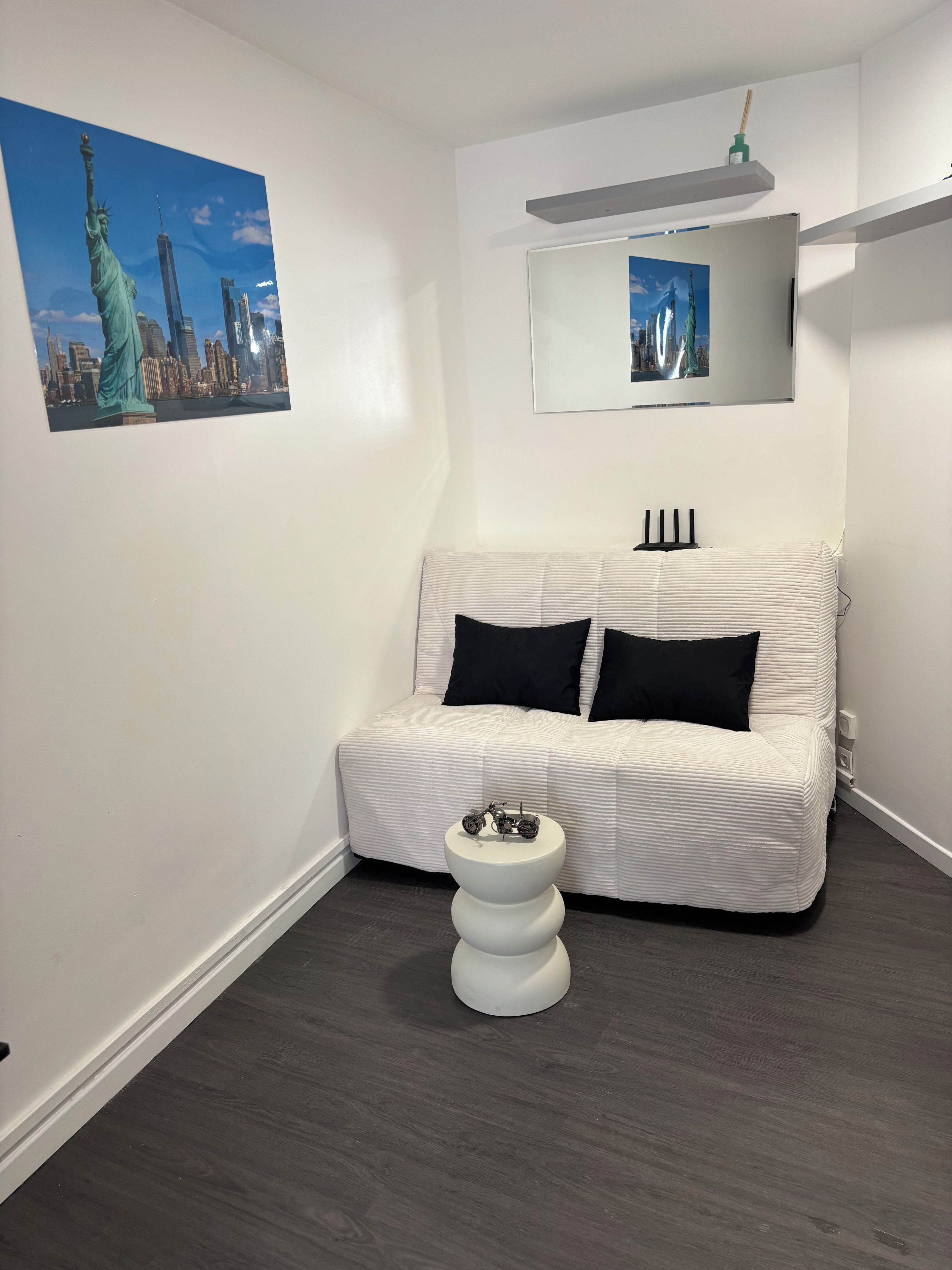 Una habitación con un sofá blanco, una mesa redonda blanca, un espejo y dos cuadros con imágenes de la Estatua de la Libertad.