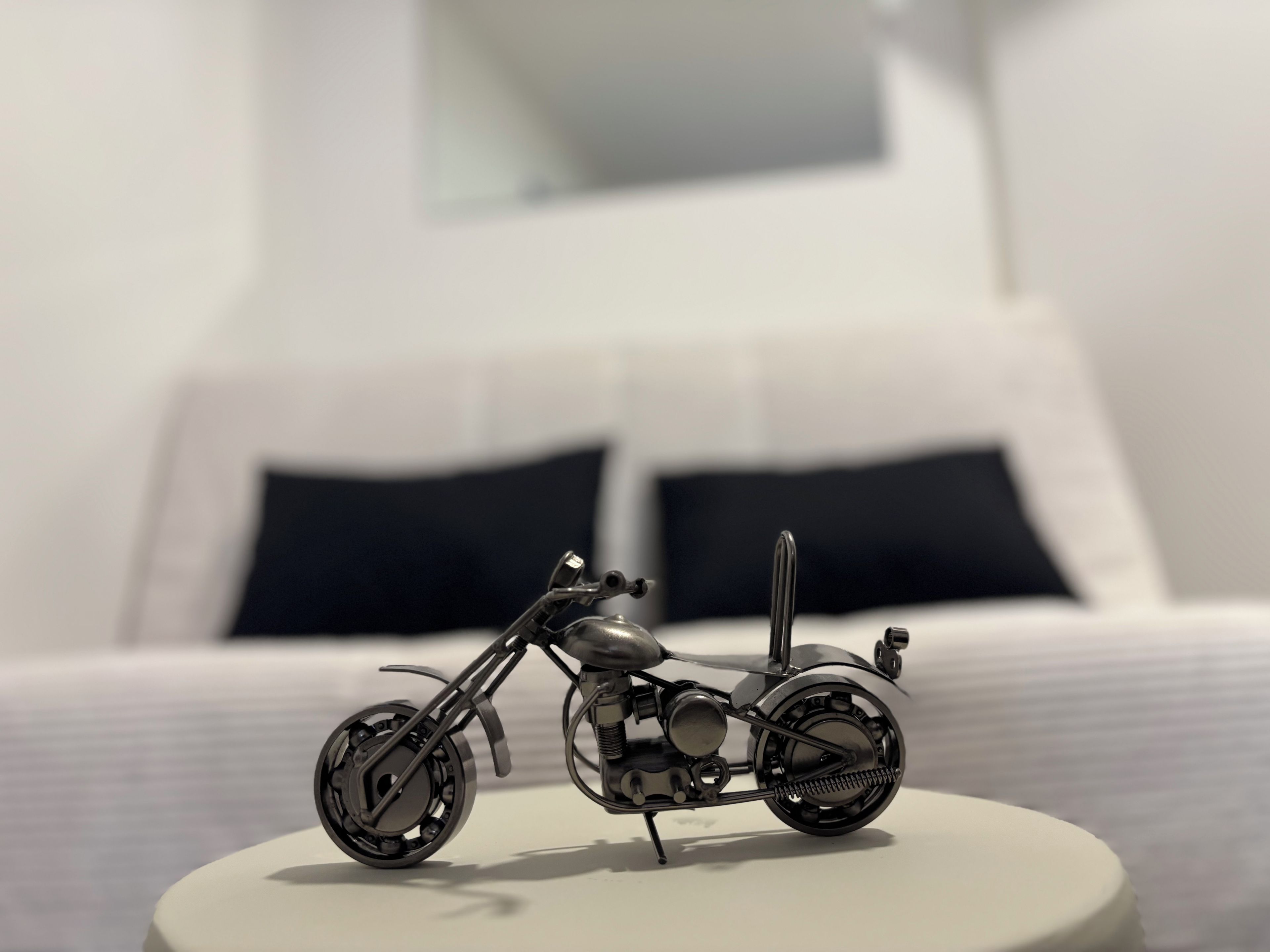 A motorcycle model on a white stand in a room with a bed and pillows.