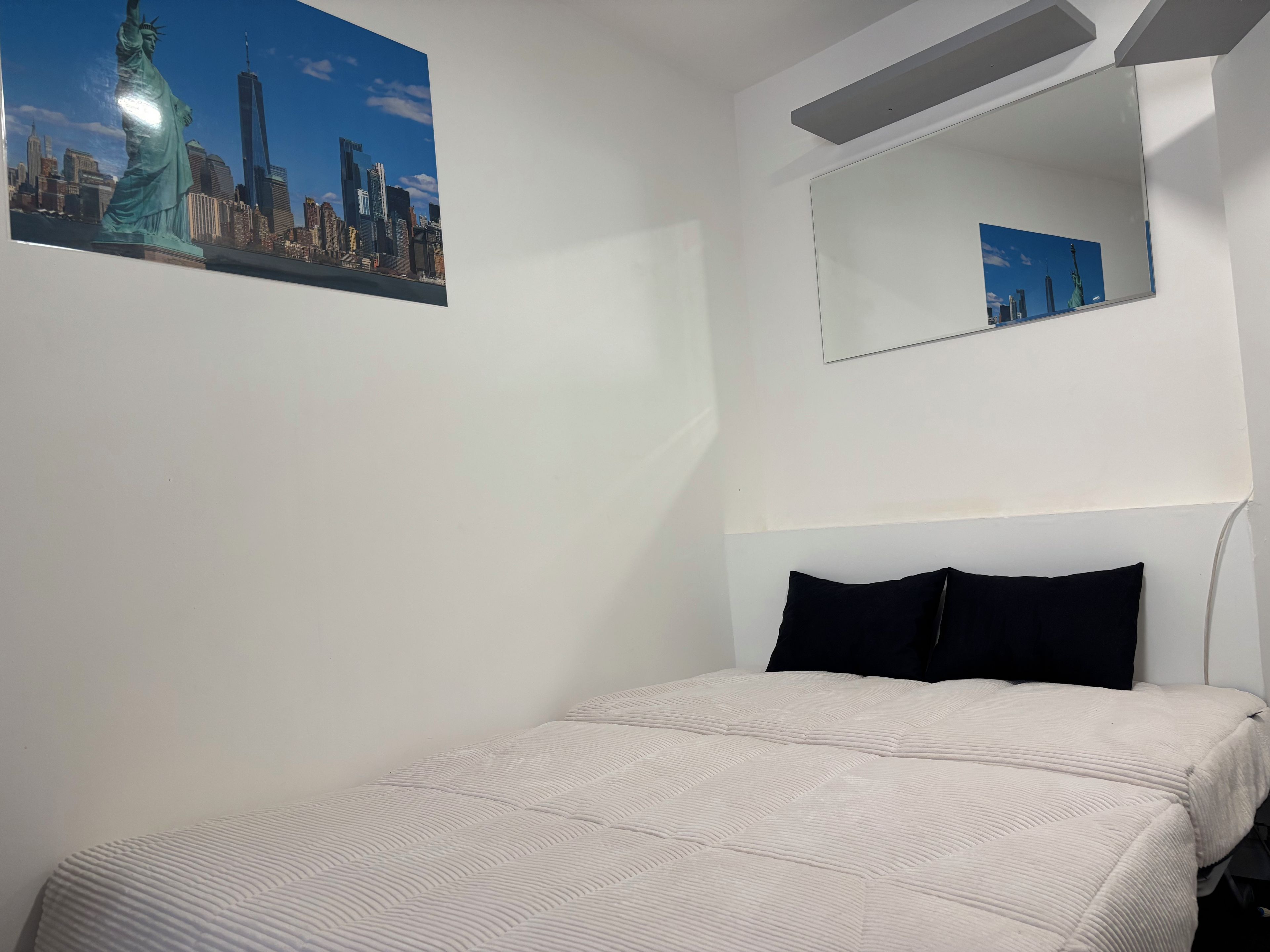 A room with a bed, a cityscape poster, a mirror, and a white wall.
