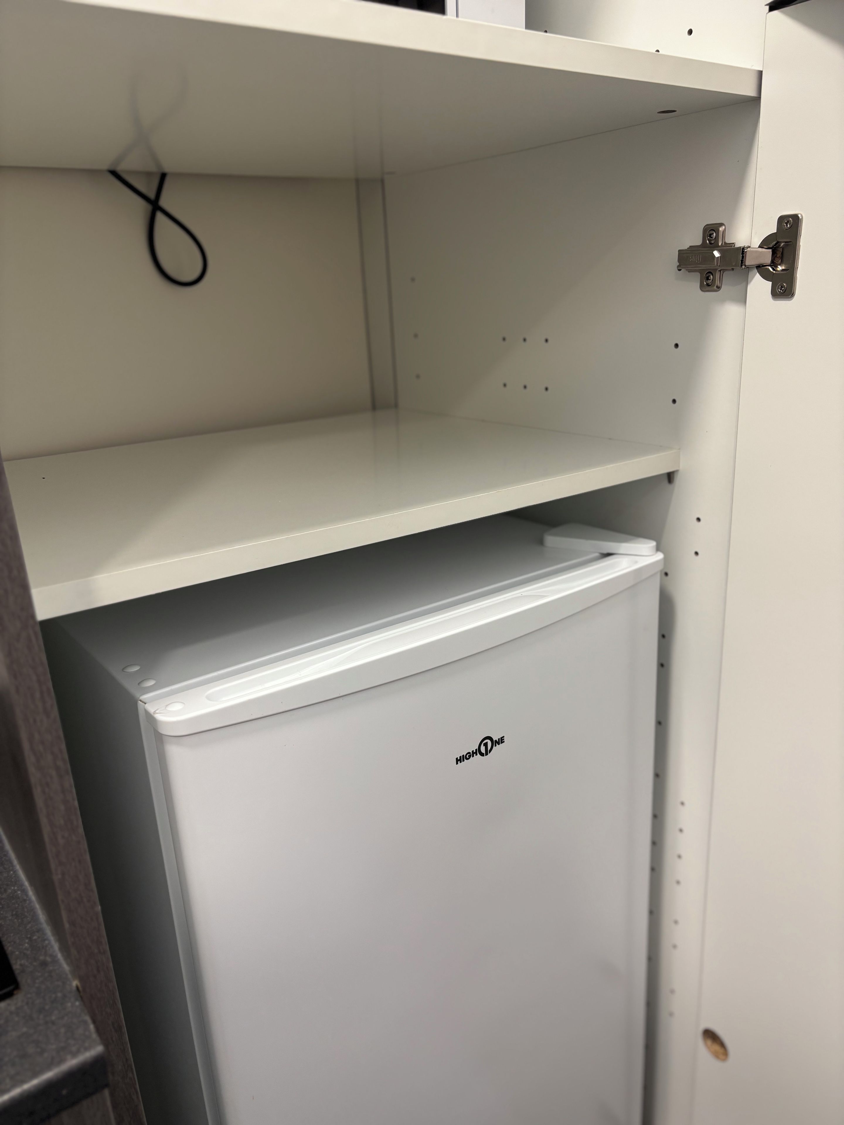 Un armario blanco con puerta abatible, un electrodoméstico blanco debajo y un cable colgando de arriba.