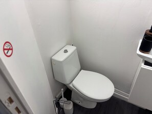 Un baño pequeño y blanco con inodoro, bidé y un cubo de basura.