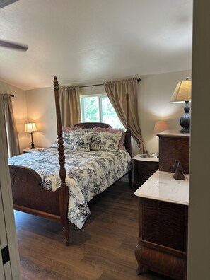 A bedroom with a four-poster bed, a nightstand with a lamp, and a dresser with a mirror. - Charming 3-Bdrm home overlooking the Majestic Coos River with AC. (Coos Bay)