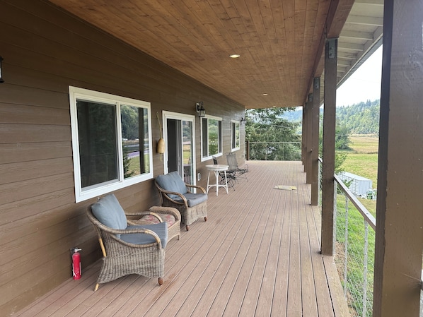 A covered deck with wicker furniture and a fire extinguisher. - Charming 3-Bdrm home overlooking the Majestic Coos River with AC. (Coos Bay)