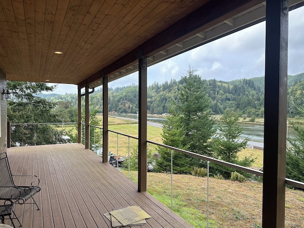 A covered outdoor deck with a view of a river and forest. - Charming 3-Bdrm home overlooking the Majestic Coos River with AC. (Coos Bay)