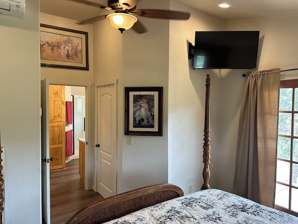 A bedroom with a bed, a ceiling fan, a mounted TV, and a window with curtains. - Charming 3-Bdrm home overlooking the Majestic Coos River with AC. (Coos Bay)