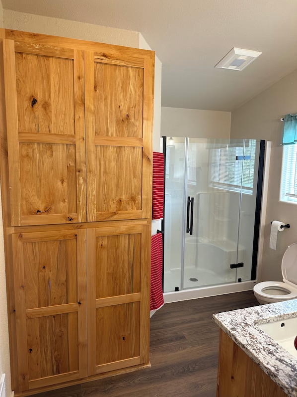 A bathroom with wooden cabinets, a glass shower enclosure, and a marble sink. - Charming 3-Bdrm home overlooking the Majestic Coos River with AC. (Coos Bay)