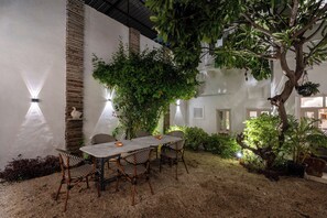 An outdoor patio with a table and chairs, surrounded by plants and a tree. - Heli Udaipur - A Century-Old Haveli (Udaipur)