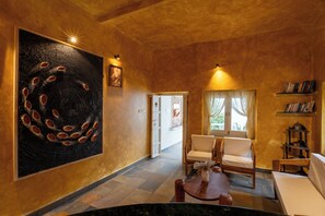 A hallway with a large abstract painting, a wooden bench, a sofa, and a bookshelf. - Heli Udaipur - A Century-Old Haveli (Udaipur)
