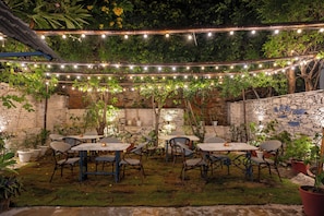 Un espacio al aire libre con mesas, sillas, luces colgantes y plantas en macetas.