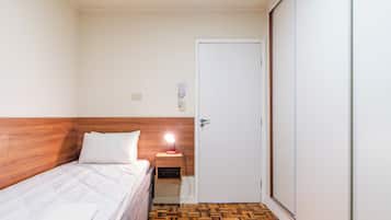 Et hotelværelse med sengegavl i træ, seng med hvide sengetøj, et natbord med lampe og en dør.