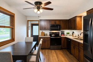 A modern kitchen with wooden cabinets, a black refrigerator, a microwave, and a stove. - Fox Valley Family Den | Sleeps 6 (Appleton)