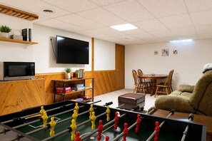 A room with a foosball table, a television, a dining table with chairs, and a sofa. - Fox Valley Family Den | Sleeps 6 (Appleton)