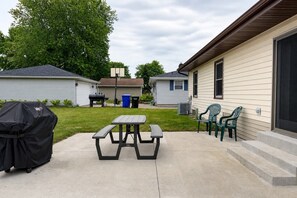 A patio with a picnic table and chairs, a barbecue grill, and a trash can. - Fox Valley Family Den | Sleeps 6 (Appleton)
