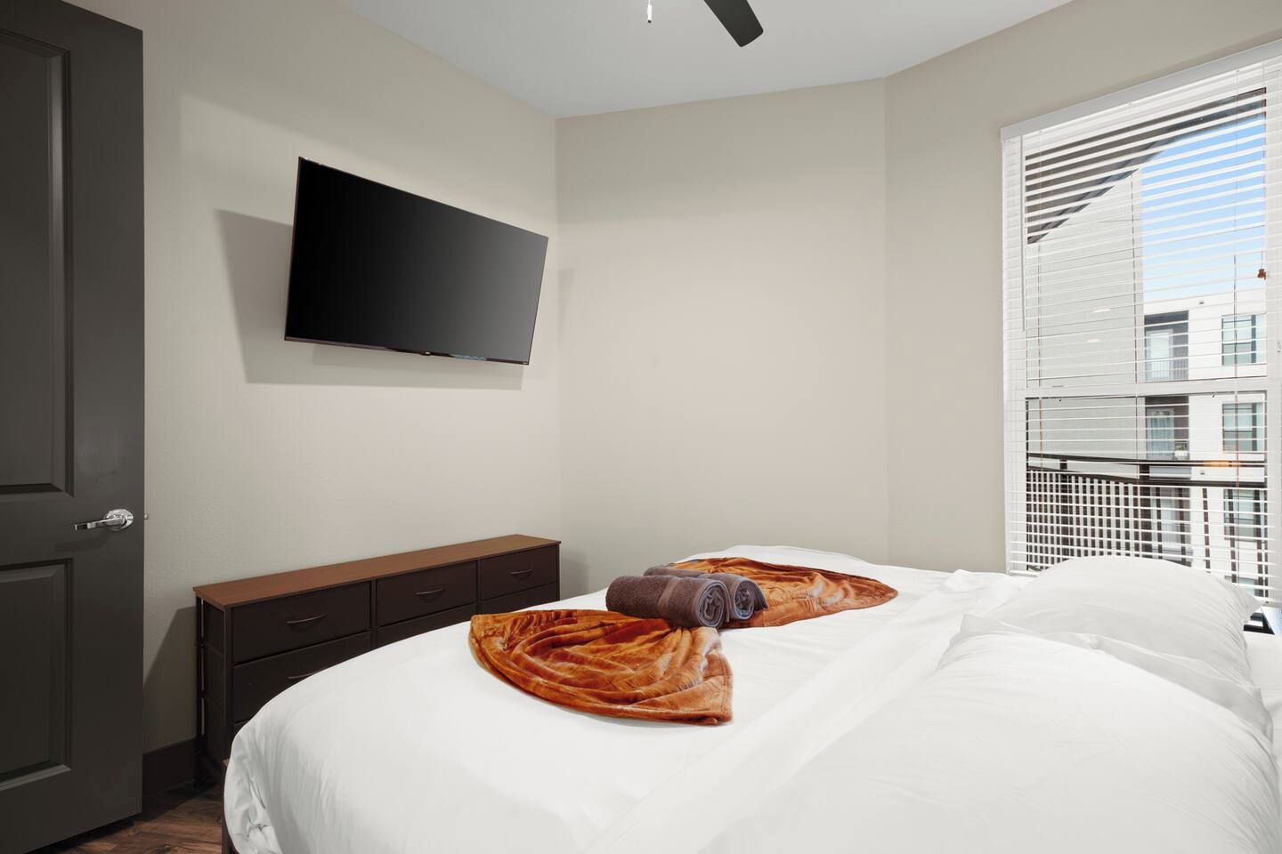 Een hotelkamer met een bed, een flatscreen televisie aan de muur, een donker houten dressoir en een raam met zonwering.