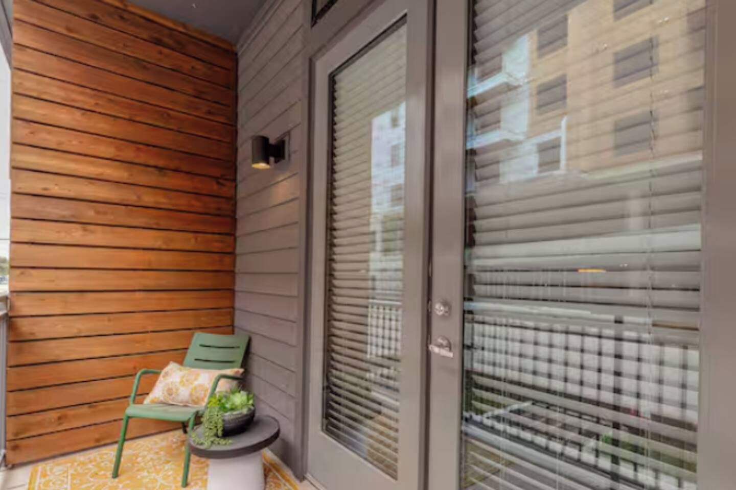 Pared exterior de madera, puerta corredera de vidrio y un pequeño espacio al aire libre con una silla y una mesa.