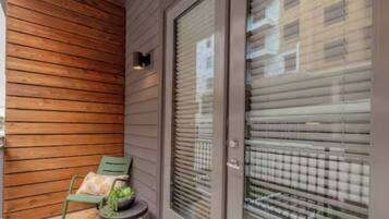 Pared exterior de madera, puerta corredera de vidrio y un pequeño espacio al aire libre con una silla y una mesa.