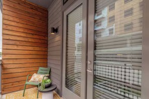 Pared exterior de madera, puerta corredera de vidrio y un pequeño espacio al aire libre con una silla y una mesa.