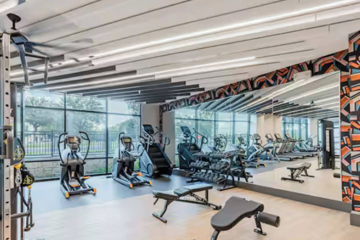 Un gimnasio con diverso equipamiento de ejercicio, amplias ventanas y un diseño moderno.