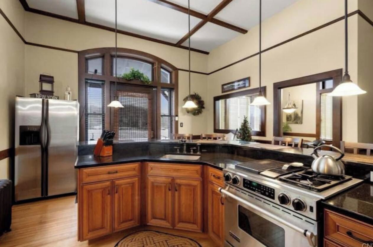 Cucina con isola centrale, elettrodomestici in acciaio inossidabile, mobili in legno e illuminazione a sospensione.