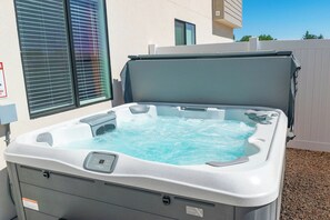 A hot tub with a control panel, set against a white fence and a building with windows. - Private hot tub| EV Charger| Near Zion| Sleeps 8 (Kanab)