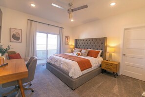 Une chambre à coucher comprenant un lit, des tables de chevet, un bureau, une chaise, un ventilateur de plafond et une porte.