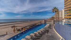 Ein Poolbereich mit Liegestühlen und Blick auf Strand und Meer.