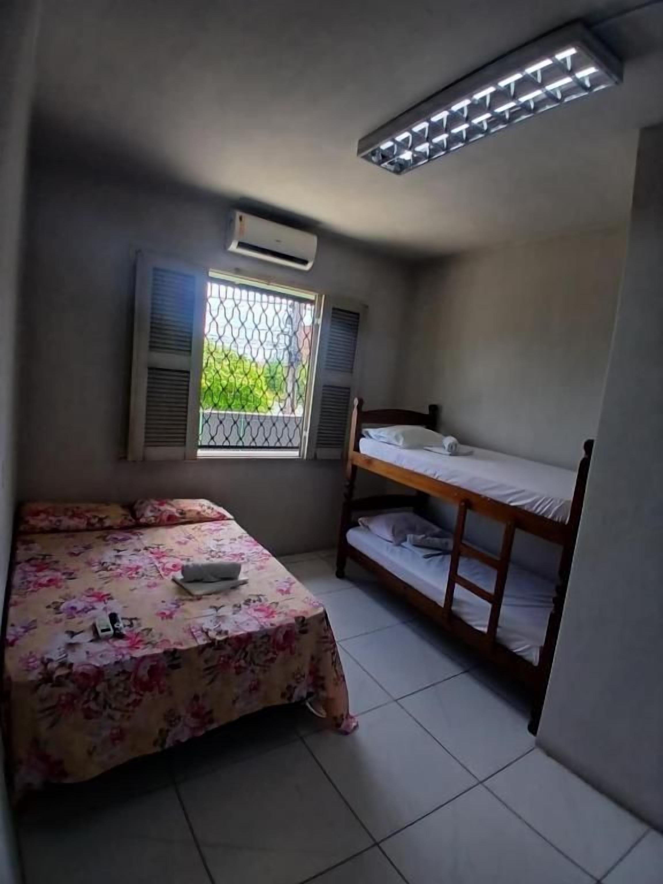 Quarto com beliche, cama de solteiro, janela com persianas e ar condicionado.