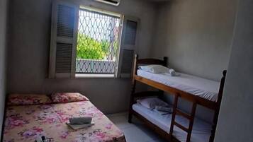 Quarto com beliche, cama de solteiro, janela com persianas e ar condicionado.