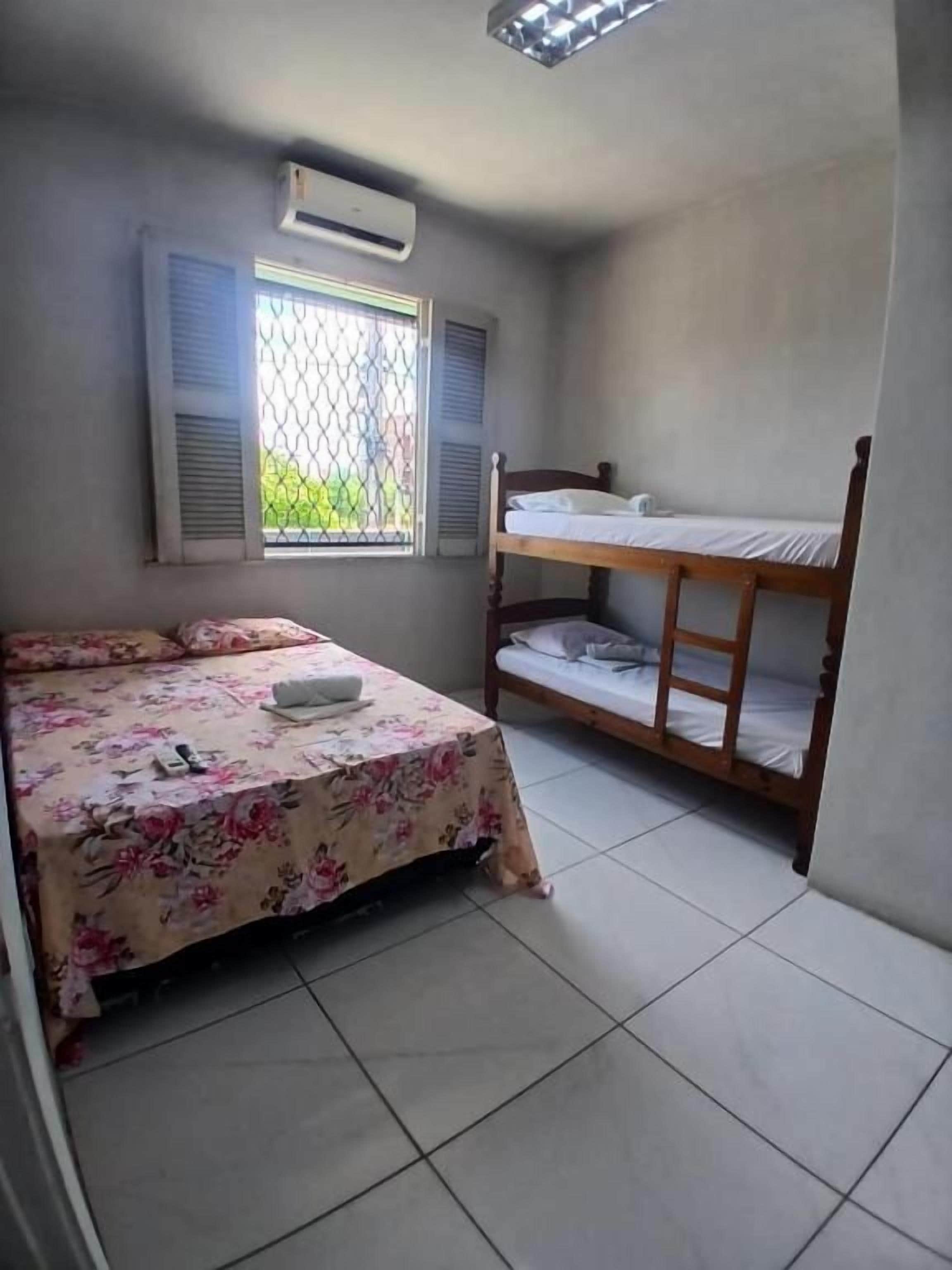 A room with a bed, a bunk bed, a window with shutters, and an air conditioning unit.