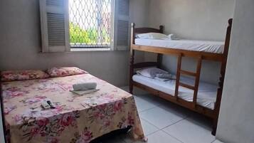 A room with a bed, a bunk bed, a window with shutters, and an air conditioning unit.
