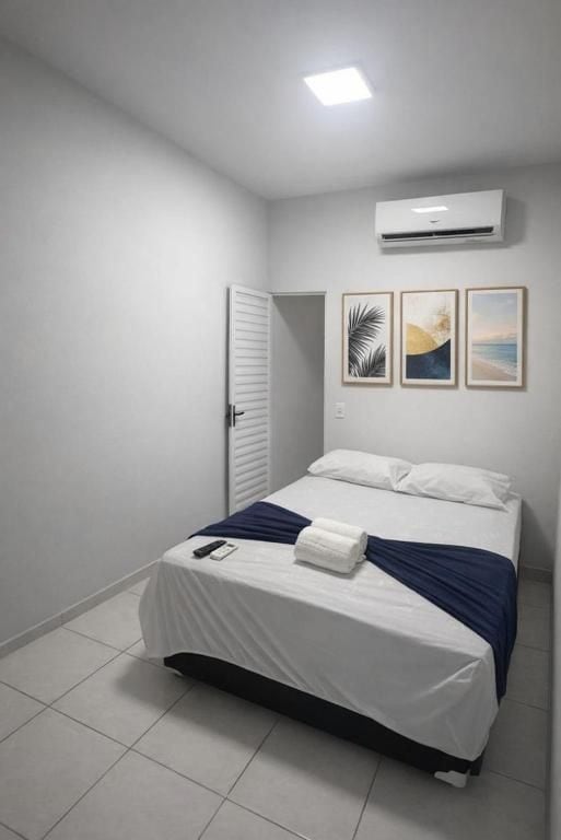 A bedroom with a bed, white walls, a door, and an air conditioner.