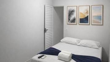 A bedroom with a bed, white walls, a door, and an air conditioner.