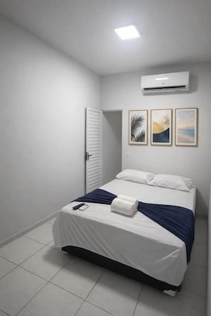 A bedroom with a bed, white walls, a door, and an air conditioner. - Pousada da paz (Fortaleza)
