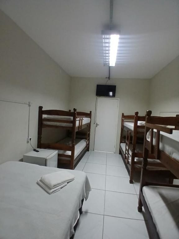 A room with bunk beds, a television, a white door, and a tiled floor.