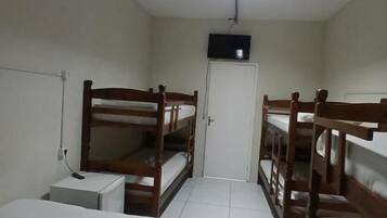 A room with bunk beds, a television, a white door, and a tiled floor.