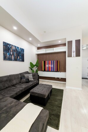 Un saló modern amb un sofà modular, una televisió de pantalla plana i una pintura de paisatge urbà.
