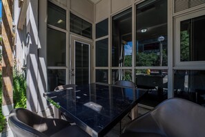 Zona d'estar exterior moderna amb un panell de vidre, una taula de marbre negre i cadires de pell.