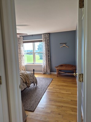 A bedroom with a bed, a wooden bench, a window with curtains, and a view of a green field. - Peaceful Country 3 Bedroom Home near Martinsburg, Shepherdstown and Hagerstown. (Martinsburg)