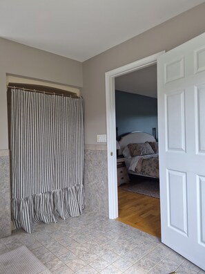 A room with a bathroom featuring striped curtains, a tiled floor, and a bed with a floral bedspread. - Peaceful Country 3 Bedroom Home near Martinsburg, Shepherdstown and Hagerstown. (Martinsburg)