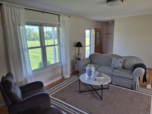 A living room with a checkered sofa, a round coffee table, and a window with curtains. - Peaceful Country 3 Bedroom Home near Martinsburg, Shepherdstown and Hagerstown. (Martinsburg)