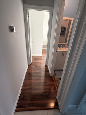 A hallway with wooden flooring leading to a bathroom with a sink and mirror.