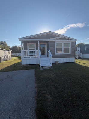 A single-story mobile home with a front porch, a small front yard, and a clear sky. - Charming 3-bedroom house with AC in Elkridge awaits you (Elkridge)